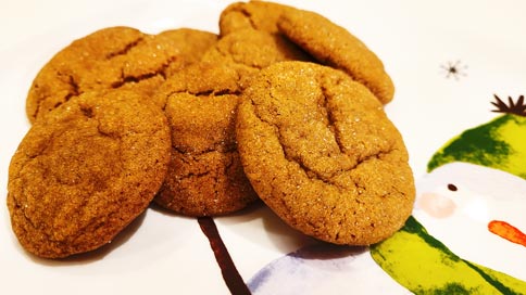 Golden brown cookies with cracks and sugar sparkle on a white plate that features a green-hatted and green-scarf wearing snowman.