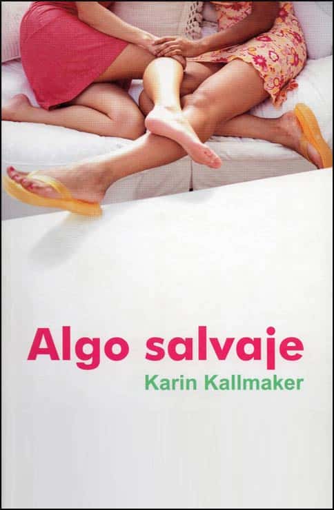 Algo salvaje by Karin Kallmaker. two young women with their legs entwined cuddle on a white sofa. Spanish language version of Wild Things.