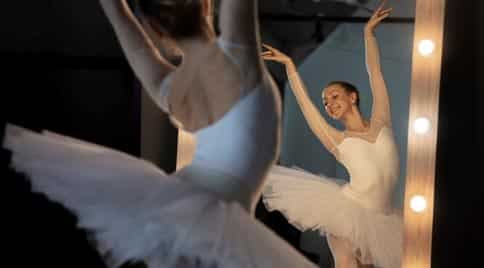 young white ballerina in white tutu on tiptoes in front of practice mirror