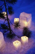 white candles with green bough against blue and white snow
