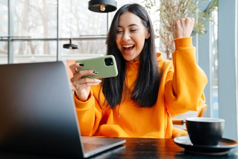 woman making excited winner gesture while looking at cell phone in a coffee shop