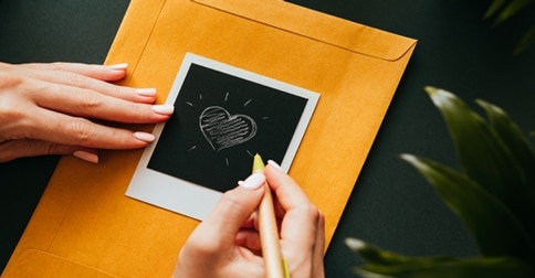 woman drawing heart on large envelope