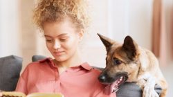 woman reading book with dog looking over her shoulder